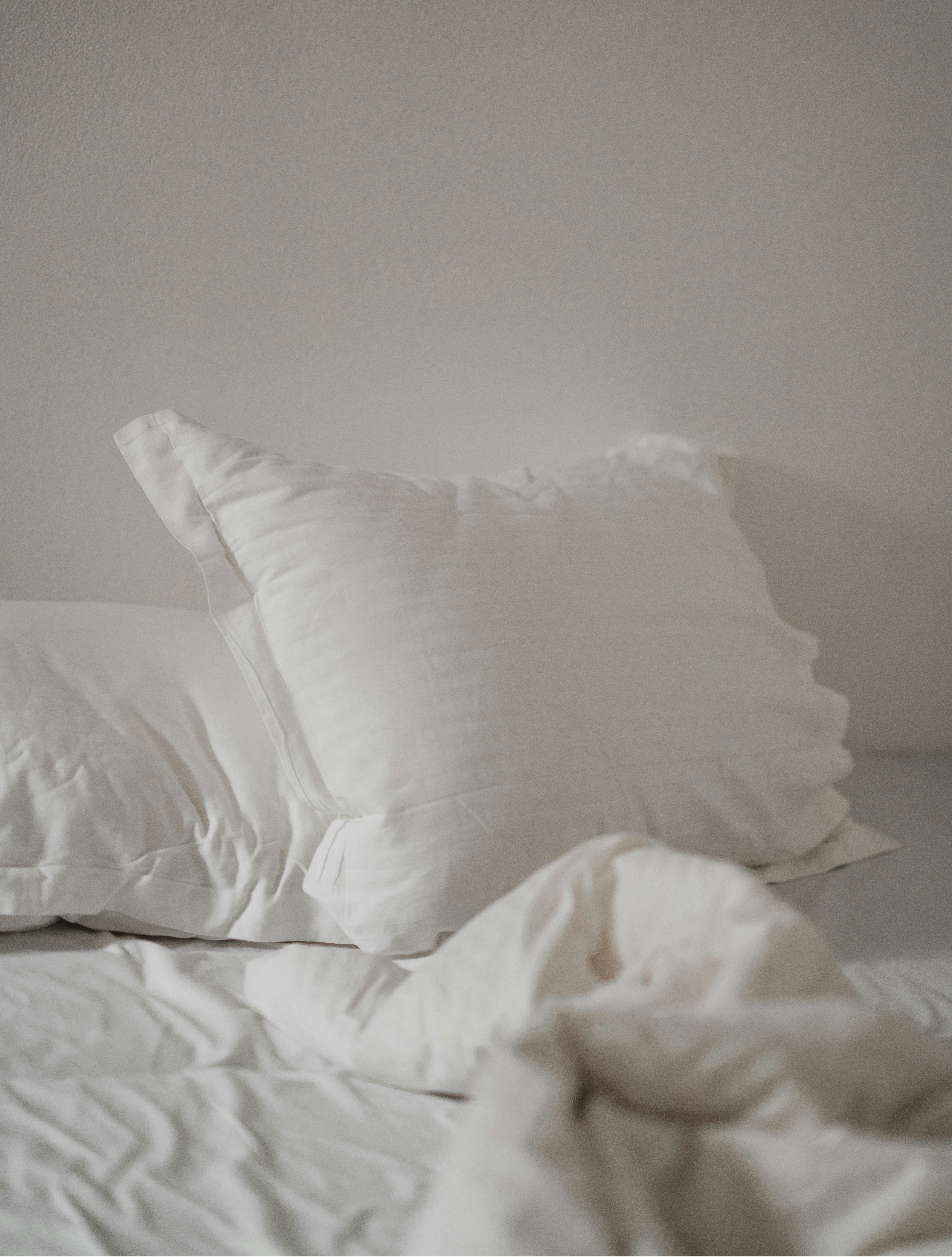 A simply made bed with linen sheets, soft morning light coming through a curtain, no clutter