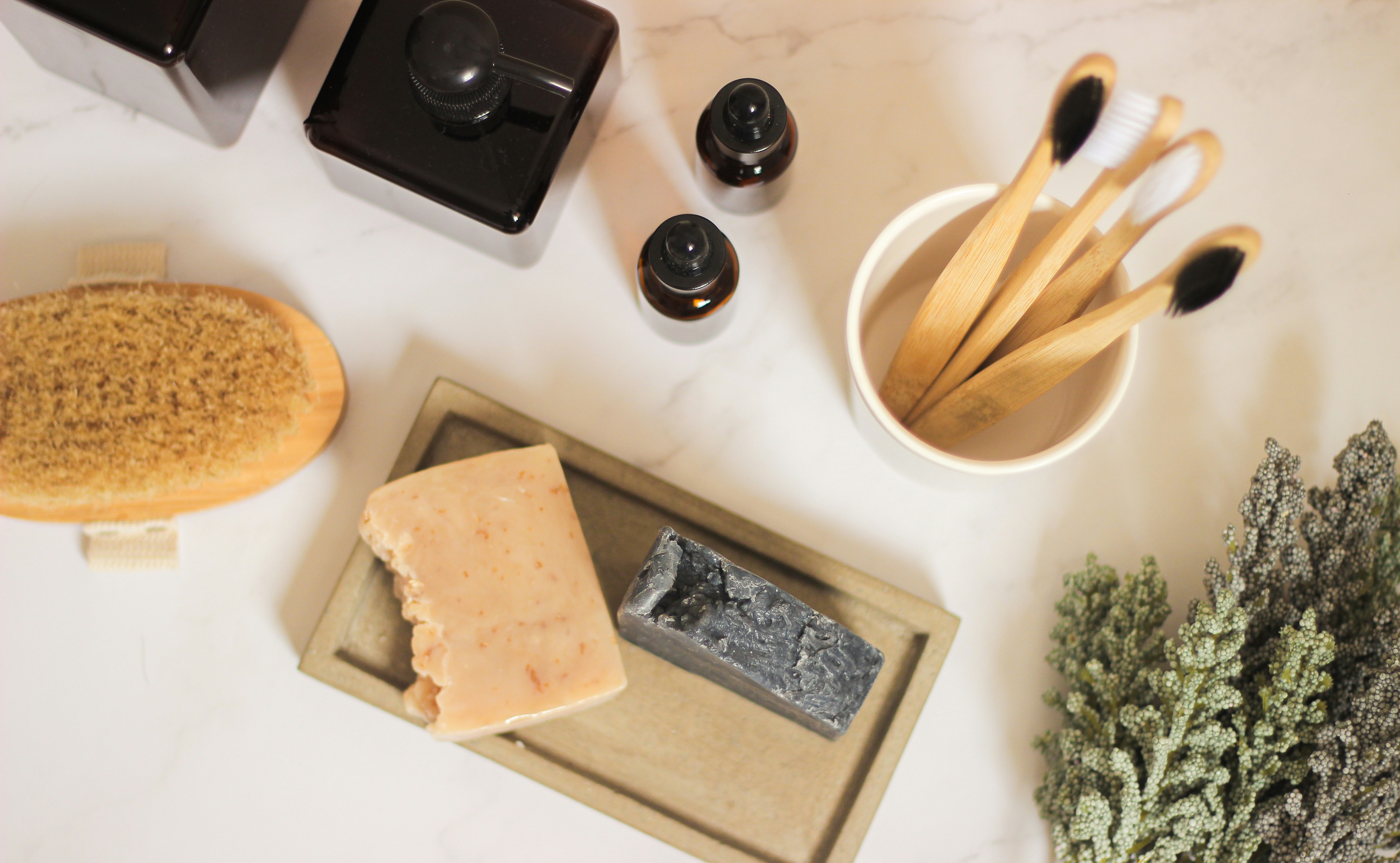 A few small glass bottles, a bar of soap and a sprig of botanical on pale linen, calm and unbranded